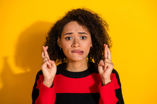 Young woman with crossed fingers in a bold striped sweater against a bright yellow background