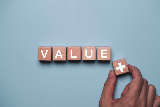 VALUE wording on block with a hand placing a plus symbol on a blue background, represent added value, business growth, customer satisfaction, branding, quality improvement, and competitive advantage.