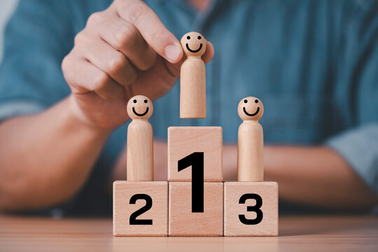 Hand placing a smiling wooden figure on the first-place podium, symbolizing leadership, employee recognition, talent management, career success, motivation, achievement, promotion and team excellence.