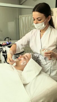 Cosmetologist applies cleansing foam to a teenage girl's face in a beauty clinic, professional skincare, gentle purification, healthy skin treatment.