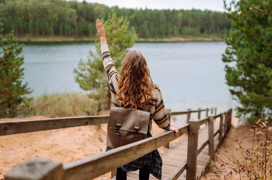 A female hiker with a backpack walks down wooden steps toward a lake. A smiling woman in a hat enjoys nature, a lake in the forest. Concept: nature, adventure. Lifestyle.