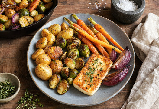 Delicious roasted vegetables and fish served on rustic plate with potatoes carrots onions brussels sprouts and herbs for a healthy meal