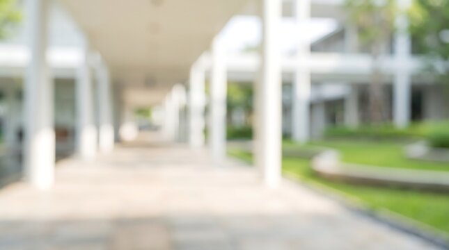 Blurred outdoor corridor of modern building with white columns and lush green garden view for architectural background concept and spacious commercial interior design presentation