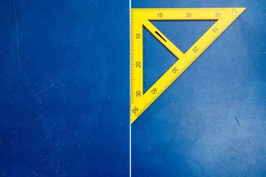 Flat lay photography of a yellow set square ruler on a textured blue surface
