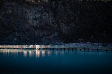 Group of tourists standing on illuminated wooden pontoon pier reflected on turquoise sulfur lake at Kawah Putih crater, Ciwidey, West Java, Indonesia. © Noer Aditia