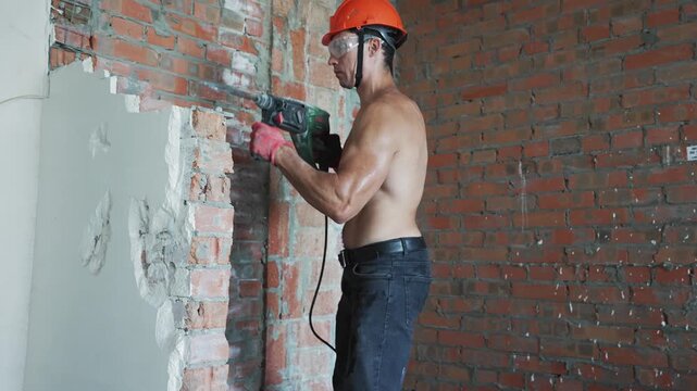 Muscular worker breaking brick wall with demolition tool in unfinished apartment. Concept of repair and construction labor.