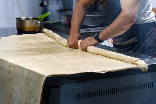 Baker Rolling Dough Sheet by Hand on Counter in Professional Bakery Kitchen