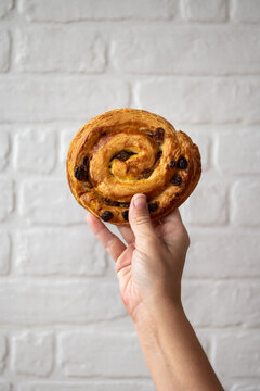Hand holding pain aux raisins against white brick wall