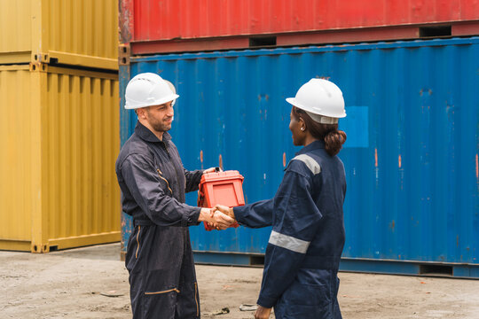 Two Engineer Workers in Safety Gear Shaking Hands and Exchanging Tool Case at Shipping Container Yard