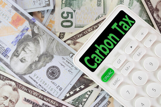 Carbon tax and environmental economics concept. White calculator displaying green Carbon Tax text on the screen, resting on US dollar bills for corporate ESG and emission penalty.