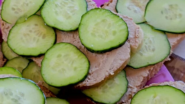 Open faced sandwiches with liver paste and fresh cucumber slices served on pink plate
