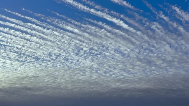 Aerial cockpit view of a layer of parallel cloud streets in a blue sky, captured at sunrise flying at 5000m high
