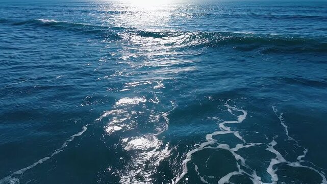 Vista a&eacute;rea del mar con intensas olas azules rompiendo en espuma blanca y destellos de luz solar sobre el agua.