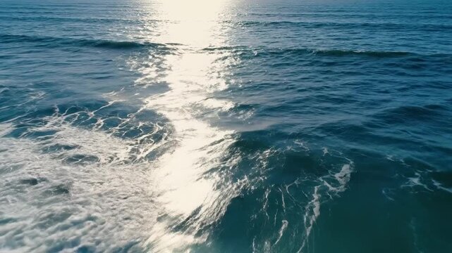 Vista a&eacute;rea del mar con intensas olas azules rompiendo en espuma blanca y destellos de luz solar sobre el agua.
