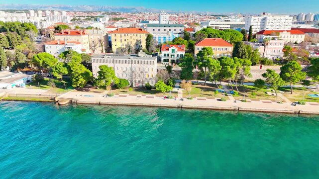 Drone flying along Zadar&rsquo;s long Kolovare promenade in spring, showing the coastline, city stretch, calm Adriatic, and distant Velebit under bright early‑season sun.