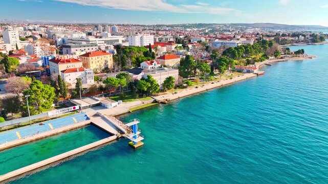 Drone sliding a half‑circle around the Kolovare jump platform and empty pool in Zadar, showing calm spring light, quiet Adriatic water, and a sunlit space waiting for summer.
