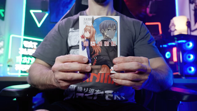 Headless person hold Japanese light novel Spice and Wolf in neon gaming room