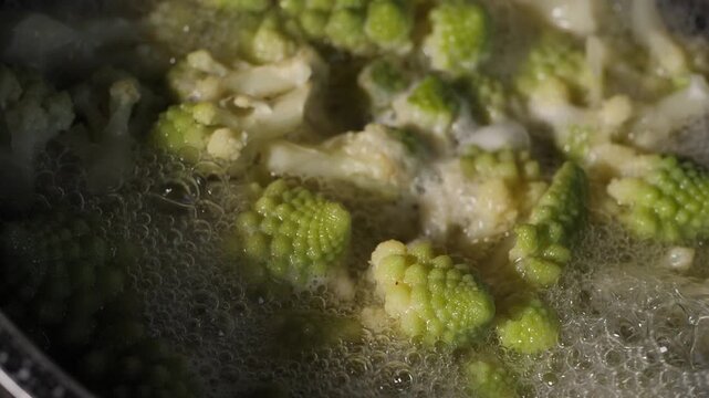 Fresh romaine cauliflower with its distinctive light green spiral florets boils in a pot of bubbling water during cooking in a home kitchen.