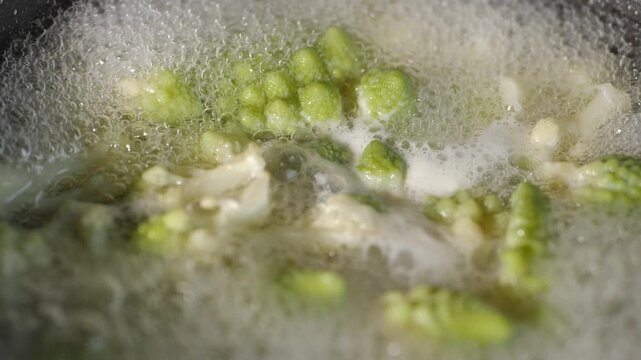 Fresh romaine cauliflower with its distinctive light green spiral florets boils in a pot of bubbling water during cooking in a home kitchen.