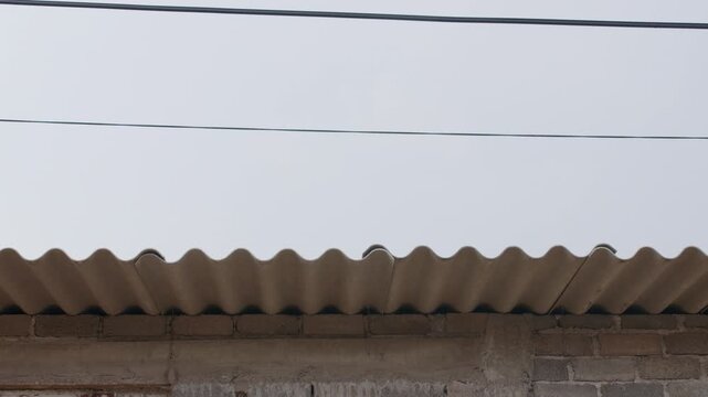Close-up of a simple concrete block home with corrugated roof, overhead wires and unfinished exterior in a modest residential neighborhood.