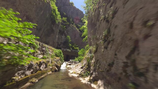 Dynamic FPV drone shot flying through a narrow rocky gorge and under a bridge in Asturias, Spain. Highlighting sustainable tourism and natural beauty.
