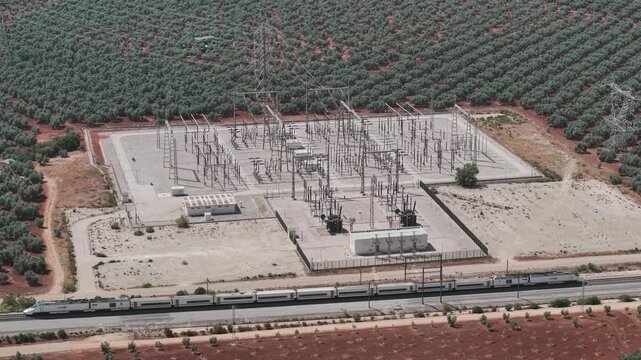 Aerial view of a high speed train traveling near a power grid station and olive groves in Spain