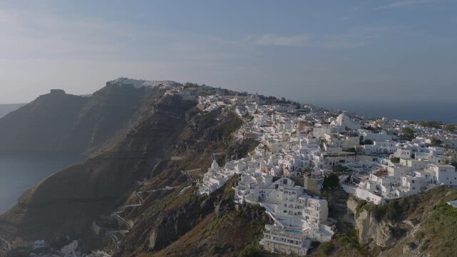 Aerial view of Fira, Santorini, with its whitewashed buildings clustered along the caldera rim above a winding switchback path down the cliffside.