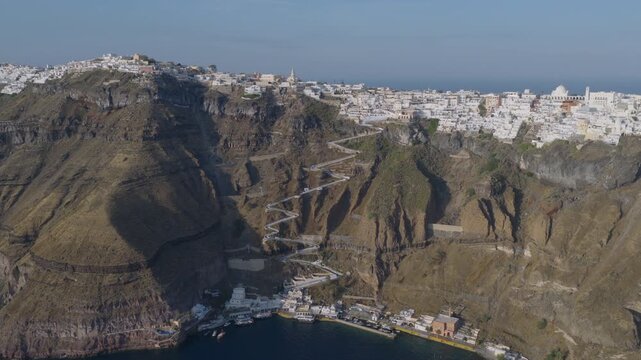 Aerial view of Santorini's steep switchback trail descending from Fira to the small harbor below, framed by dramatic caldera cliffs and the sea.