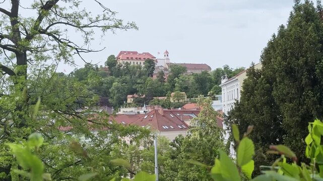 Vew of Brno Castle framed by green parkland and gently moving bushes. Wide 4K footage highlighting historic architecture and peaceful natural surroundings.