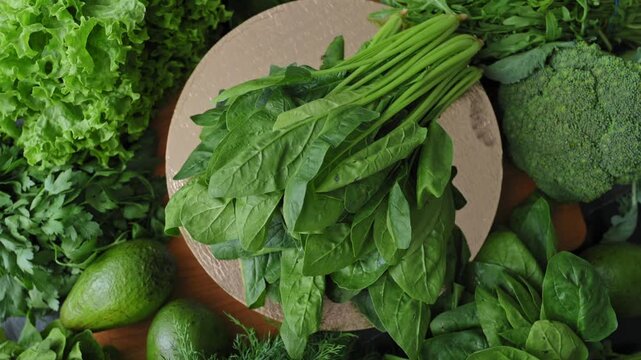 Fresh spinach rotating on golden podium beside broccoli, avocado, lettuce, parsley and dill. Spinach, leafy greens, green vegetables showcase organic produce for healthy eating and food. 4k 