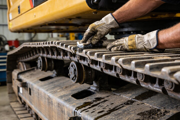 Heavy equipment mechanic cleaning excavator tracks with a rag and gloves © Snide12