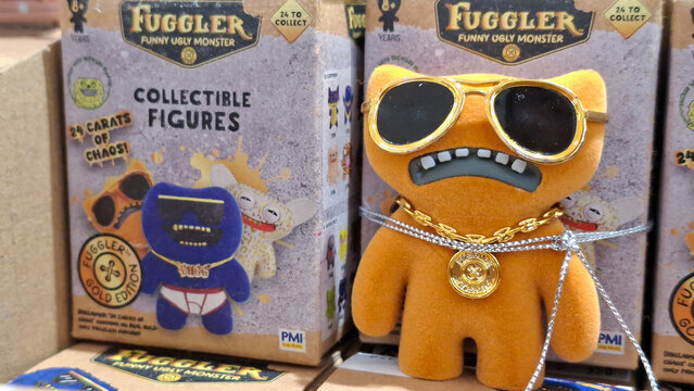 orange fuggler funny ugly monster collectible figure wearing gold sunglasses and chain necklace next to blind box packaging on June 10, 2026 in Bangkok, Thailand.