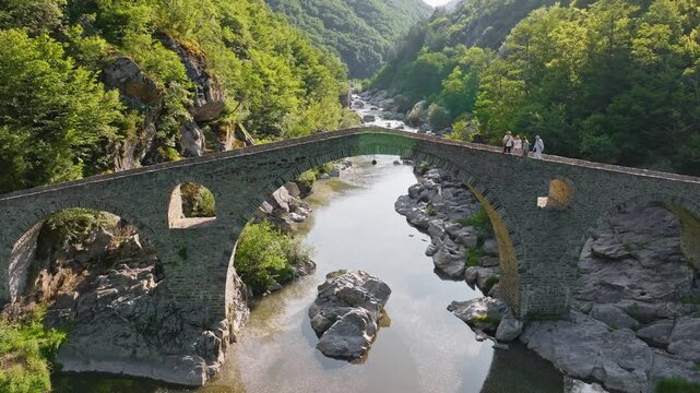 Devils Bridge aerial view with tourists walking on historic stone arch bridge over Arda River gorge in Rhodope Mountains Bulgaria summer travel destination
