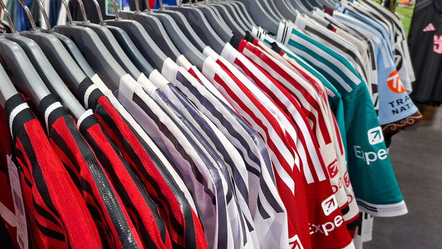 Row of various colorful football club jerseys hanging on plastic clothes hangers in modern sports retail store on June 2, 2026 in Bangkok, Thailand.
