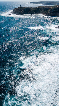 Vista a&eacute;rea del mar con intensas olas azules rompiendo en espuma blanca y destellos de luz solar sobre el agua.