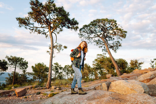 A young woman with a backpack enjoys the sunset on a mountain hiking trail. Concepts of adventure, hiking, and travel. Active lifestyle.