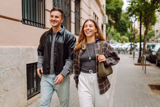 A young woman and a man walk along a busy street in a sunny city. A smiling couple strolls and talks to each other at sunset. Concepts of friendship, communication, and leisure.