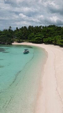 Aerial view of beach with a wide sandy shore lies beside clear turquoise coastal water. M LHuillier Beach. Camotes, Philippines.