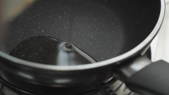 Pouring cooking oil into a black non-stick frying pan on a stove. Concept of culinary preparation, cooking meals, and kitchen background.