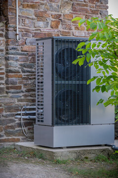 Air source heat pump installed beside a residential stone house. Energy-efficient heating and cooling system supporting sustainable home climate control, reduced energy consumption, and low-carbon.