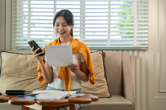 A young Asian woman with many expense bills and she using smartphone to calculate and purchase with scan qr code payment shopping online.