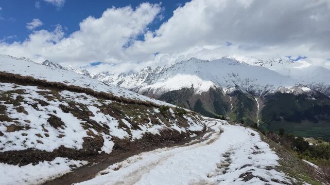 Snowy dirt road winding through Koruldi ridge in Svaneti Georgia with majestic Caucasus mountain peaks and cloudy sky