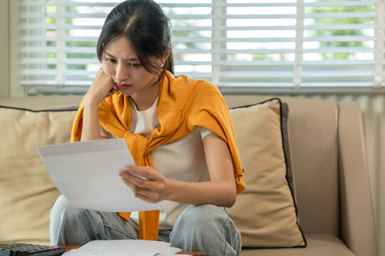 A young Asian woman is stressed because she looks at many expense bills and she has no money to pay them. Hand on head feeling serious depressed. Rising high cost of living in low poor income people