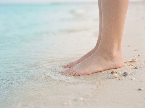 Woman standing on beach sand. Feet dipping into ocean water at the shore.