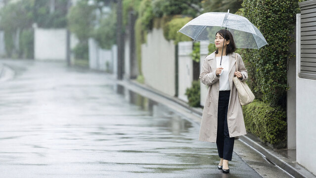 雨の朝に傘をさして通勤する日本人女性