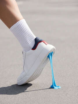 Close-up of a white sneaker with blue bubblegum stuck to the sole mid-step, providing a playful concept for youth fashion shoe campaigns