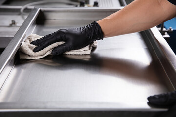 Hand in black glove wiping down a shiny stainless steel surface with a cloth © Snide12