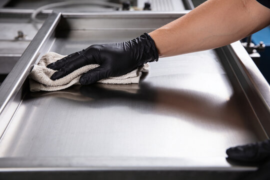 Hand in black glove wiping down a shiny stainless steel surface with a cloth