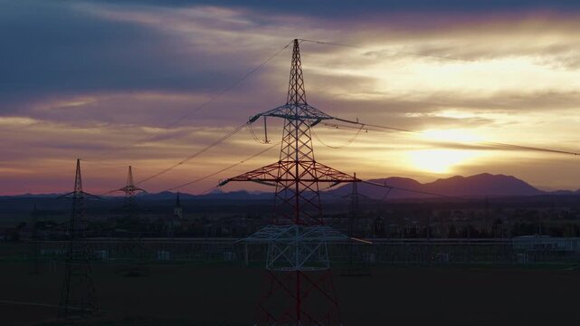 High-voltage electrical substation switchyard shows transformers and transmission lines during dramatic sunset sky in a rural area.