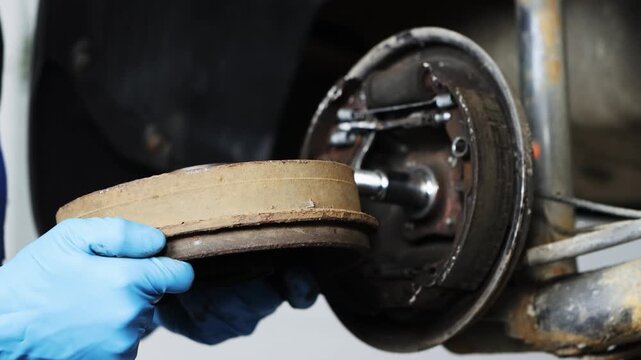 A uniformed auto mechanic repairs a car's brake system by removing the brake drum.